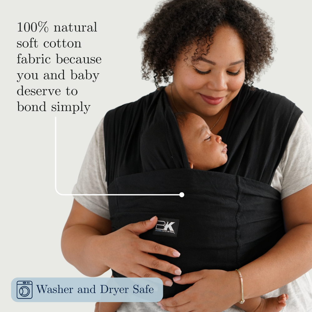 Woman holding a baby in a black baby carrier with text about natural soft cotton fabric.