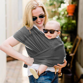 A woman cradling a baby in a gray Baby K'tan carrier, highlighting a close and caring bond.