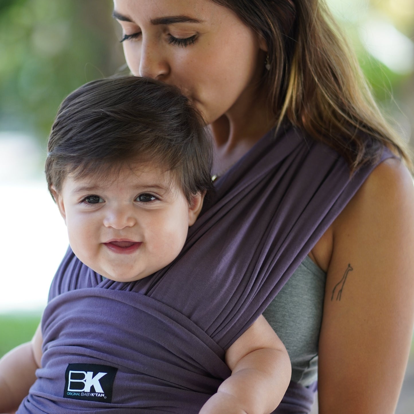 A woman with a baby secured in a purple Baby K'tan carrier, showcasing a nurturing embrace.