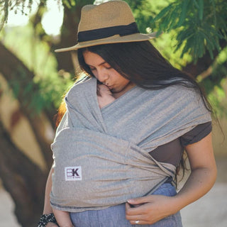A woman with a grey Baby K'tan baby carrier, securely carrying her baby in a front-facing position.