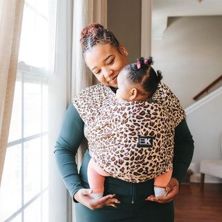 A woman holds a baby in a leopard print Baby K'tan carrier, showcasing a stylish and functional baby-wearing option.
