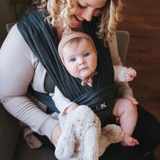 A woman with a baby secured in a black Baby K'tan carrier, showcasing a nurturing embrace.