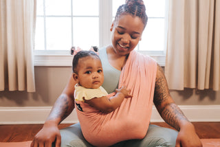 A woman holds a baby in a Baby K'tan sling, showcasing a close bond and comfortable carrying method.