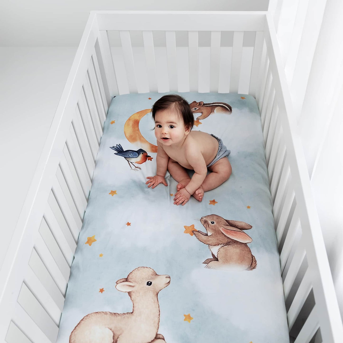 Baby sitting on a crib mattress with animal illustrations