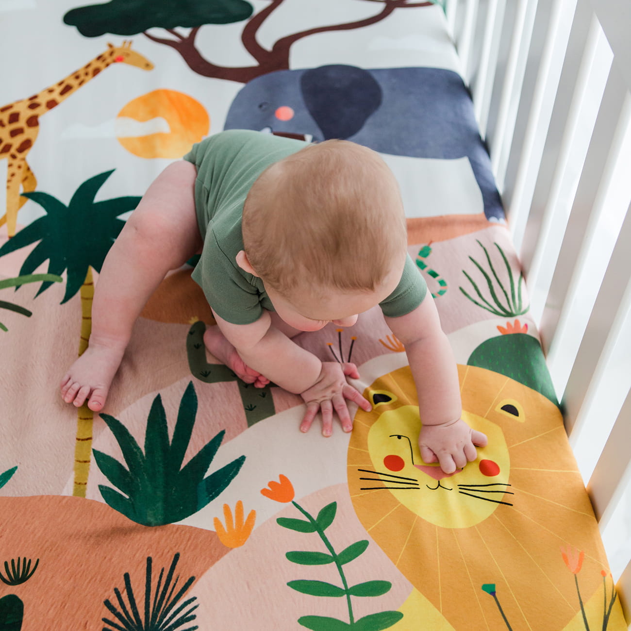 Baby playing on a colorful animal-themed mat in a crib.