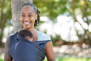 A woman in a baby carrier walks through a park, enjoying the outdoors with her child securely nestled against her.