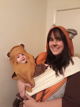 Smiling woman holding a baby, both dressed in matching Ewok costumes.