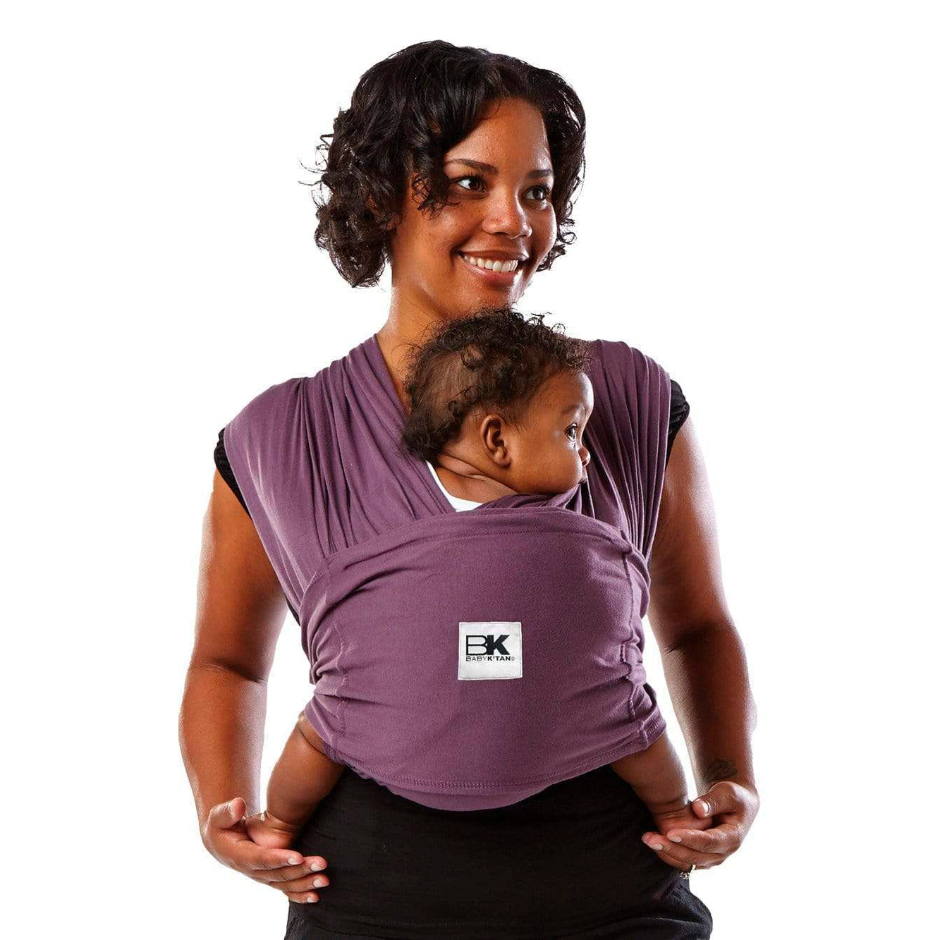 A woman wearing an eggplant-colored Baby K'tan Original Baby Carrier with a sleeping infant inside.