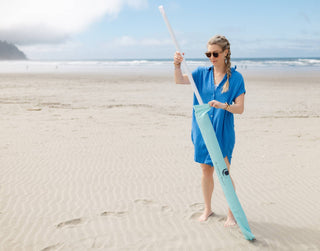 Woman holding a paddle on a sandy beach with ocean and sky in the background
