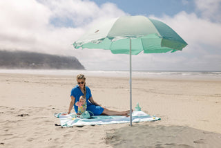 Woman with child under a green beach umbrella on a sandy beach