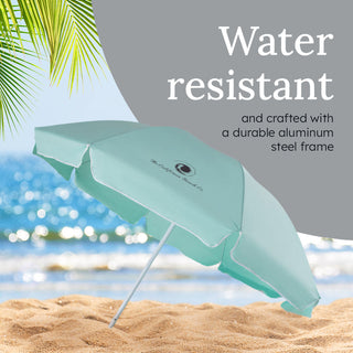 Teal beach umbrella on sand with ocean and palm tree in the background, text indicating water resistance and durable frame.