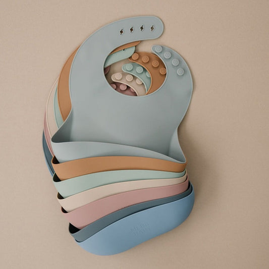 Stack of colorful baby bibs on a beige background