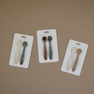 Three sets of baby spoons in packaging on a brown background