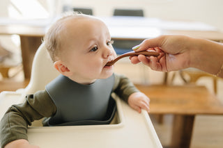 Baby in a high chair being fed with a spoon by an adult hand.