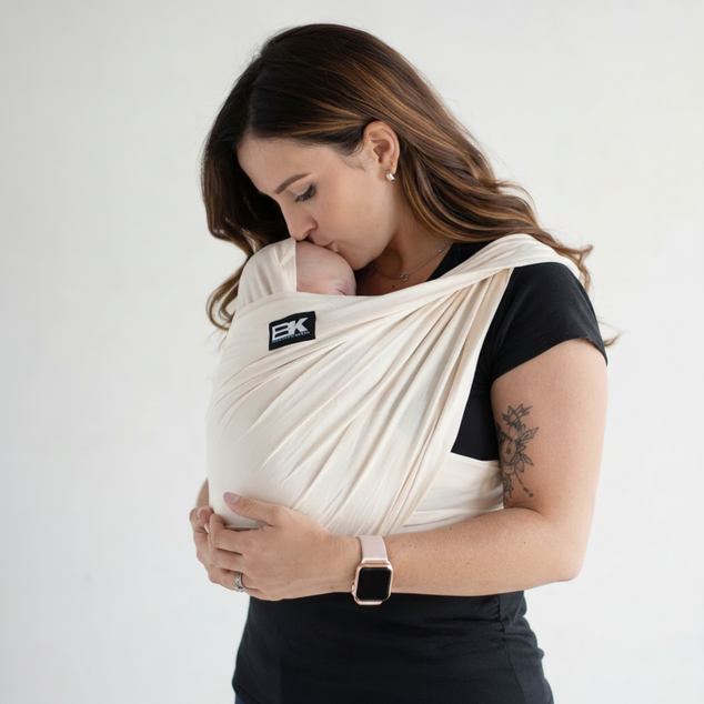 Woman wearing a baby in a sling with a visible brand logo on a plain background