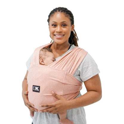 A person wearing a pink Baby K'tan Active Yoga Baby Carrier with a sleeping infant inside.