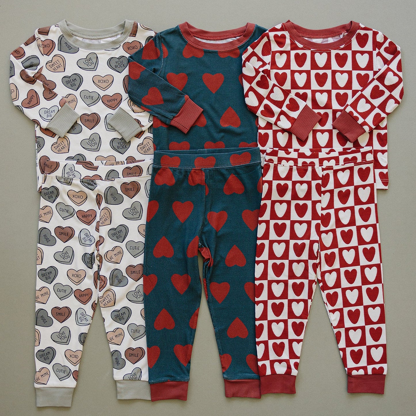 Three children's pajama sets with heart patterns on a gray background