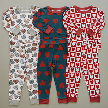 Three children's pajama sets with heart patterns on a gray background