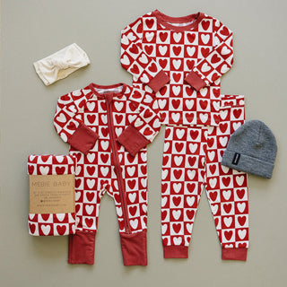 Red and white heart-patterned baby onesie with matching headband and hat on a neutral background