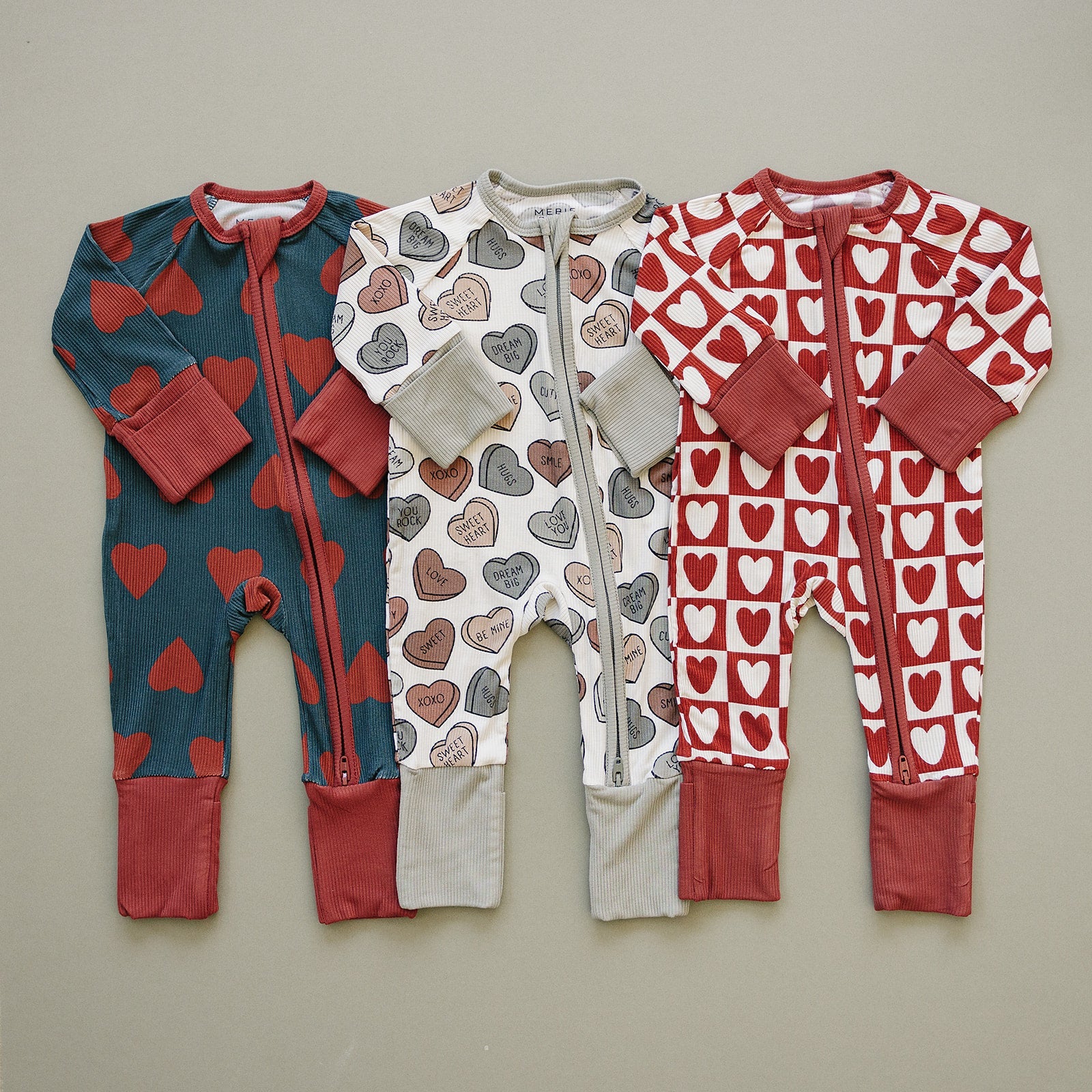 Three baby rompers with heart patterns on a beige background