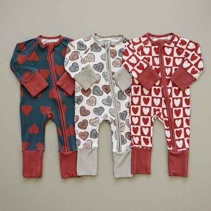 Three baby rompers with heart patterns on a beige background