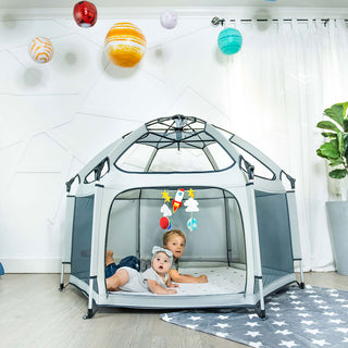 Children playing inside a dome-shaped playpen with colorful toys hanging above.