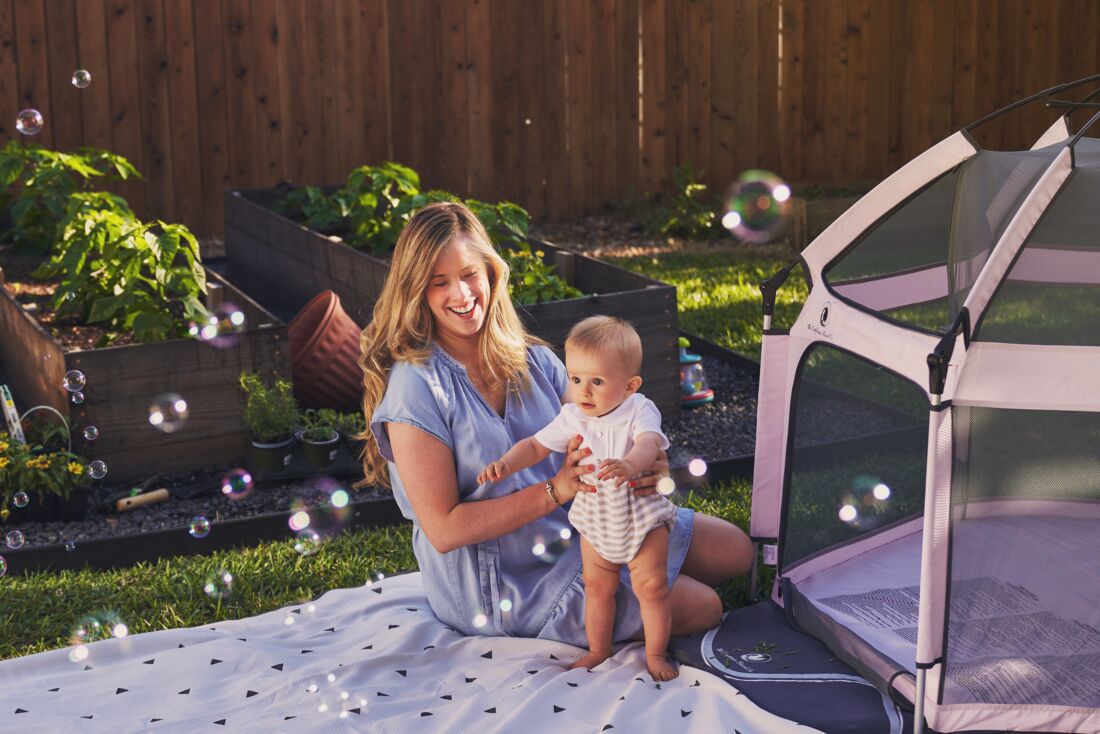 Woman holding a baby in a garden with bubbles and a tent in the background