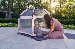 Woman and child playing with a portable playpen in a garden setting