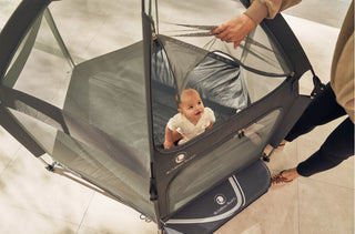 Baby in a portable playpen with a person holding it, on a light background