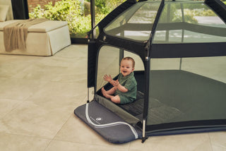 Child sitting inside a portable playpen on a tiled floor.