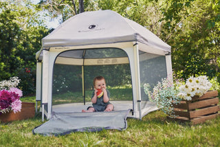Child sitting inside a portable playpen with flowers and greenery around