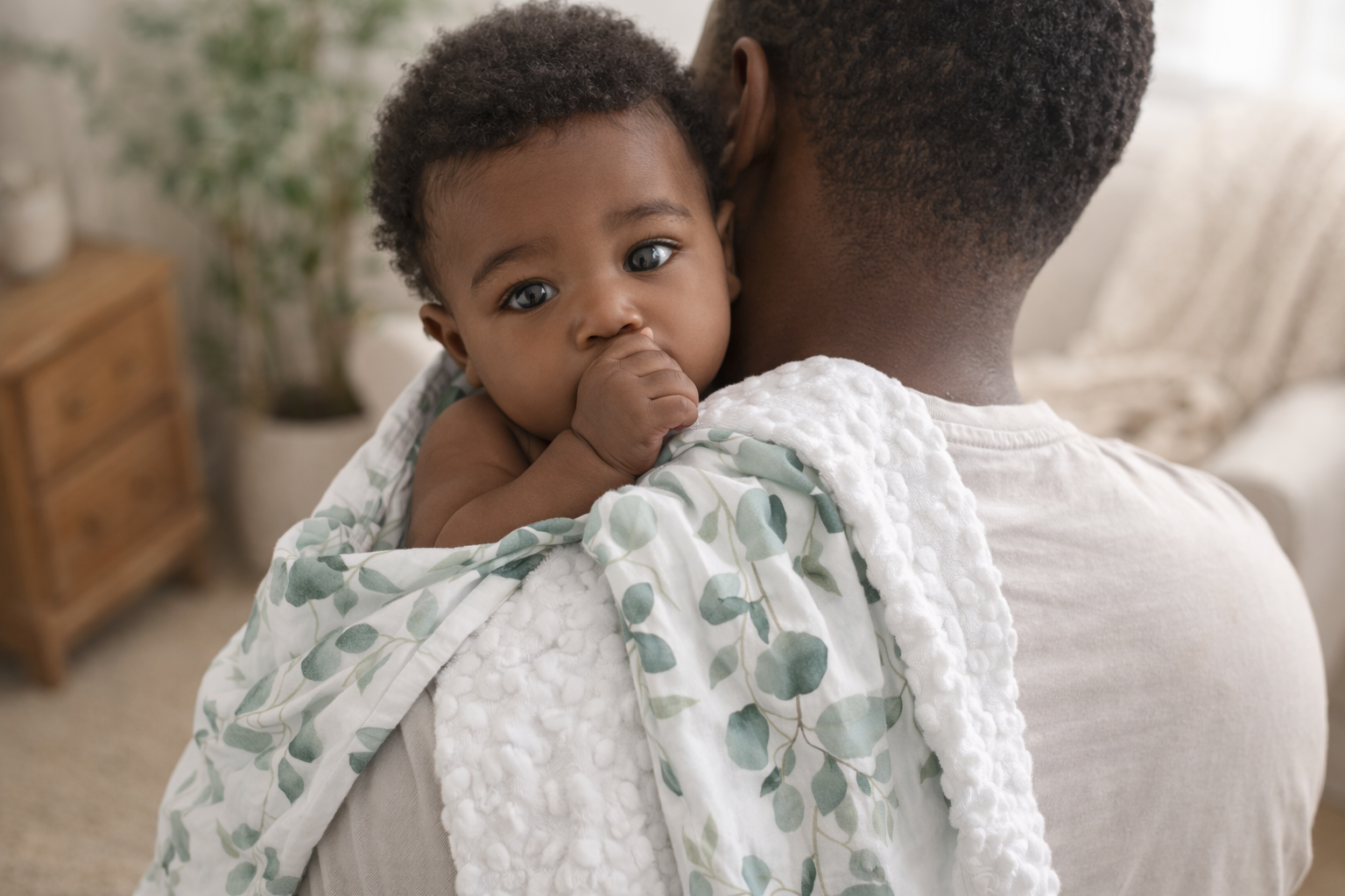 Baby wrapped in a green and white blanket held by an adult in a home setting.