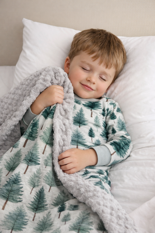 Child wrapped in a blanket with a tree pattern, lying on a bed.