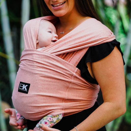 A person wearing a pink Baby K'tan Active Yoga Baby Carrier with a sleeping infant inside.