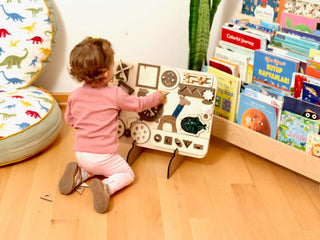 Child playing with a educational toy on the floor next to a bookshelf filled with books.