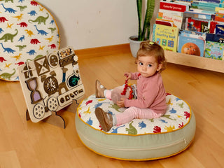 Child sitting on a colorful cushion playing with toys in a room with books and a dinosaur-themed plate.
