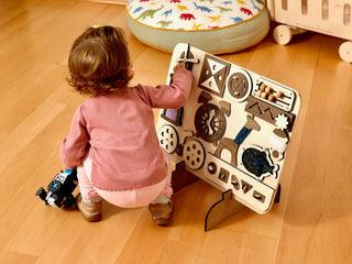 Child playing with a wooden activity board on a wooden floor
