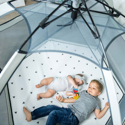 Two children lying on a white mat with black triangle patterns inside a transparent dome structure.