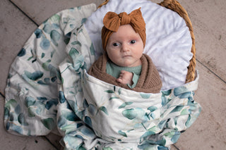 Newborn baby wrapped in a floral blanket with a headband, sitting in a woven basket.