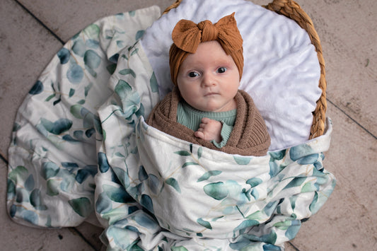 Newborn baby wrapped in a floral blanket with a headband, sitting in a woven basket.