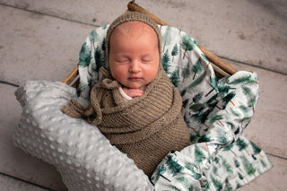 Newborn baby wrapped in brown fabric with a green and white patterned blanket