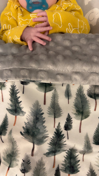 Child in yellow shirt with tree pattern holding a gray blanket with tree pattern