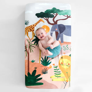 Baby sitting on a colorful safari-themed mat with animals and plants.