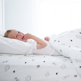 Person lying in bed with white bedding featuring black patterns