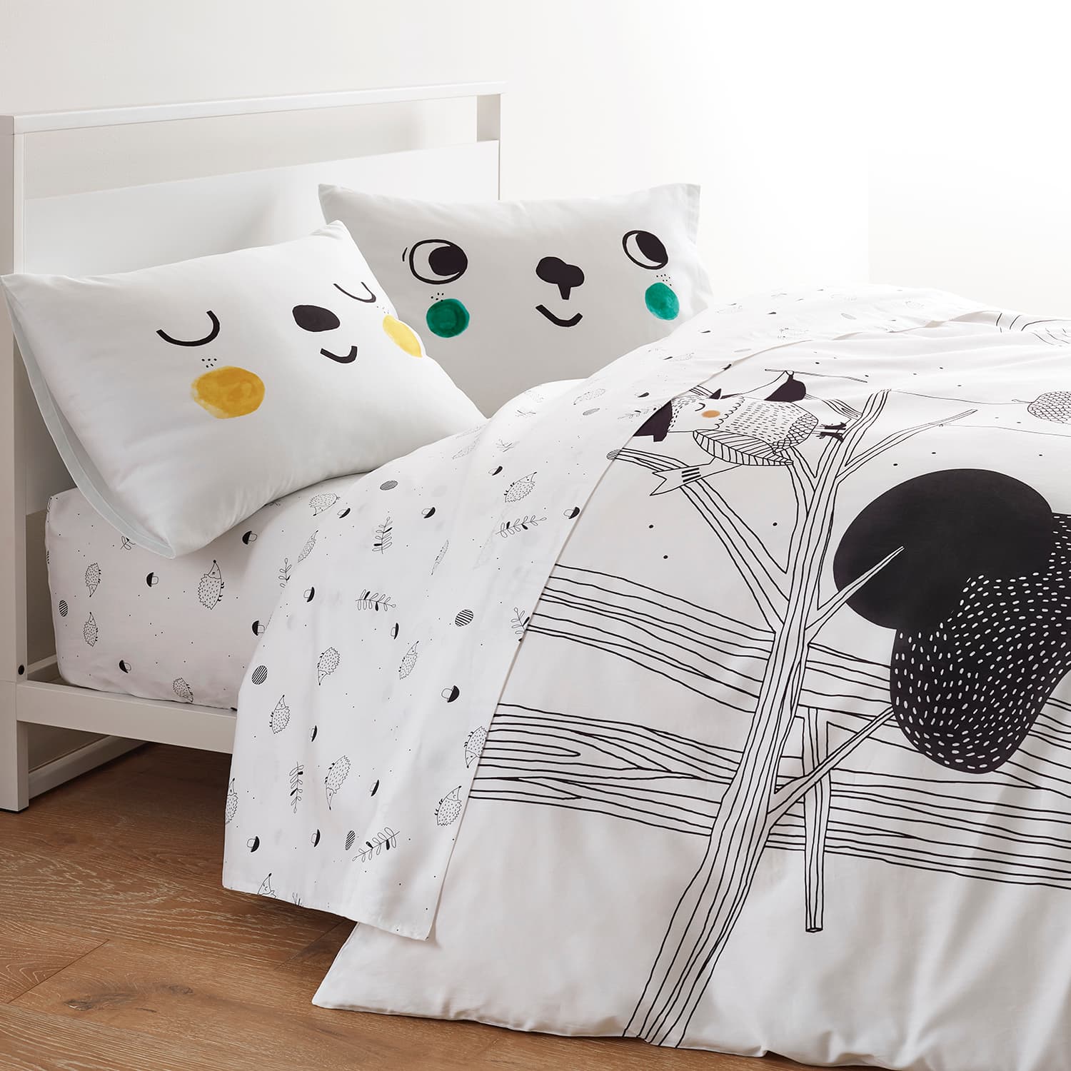 Children's bed with white bedding featuring black tree design and colorful animal face pillows.