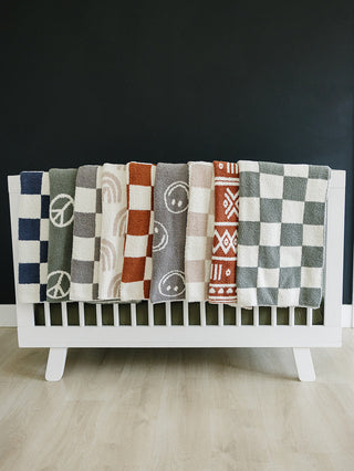 Collection of patterned blankets draped over a white crib against a dark wall.