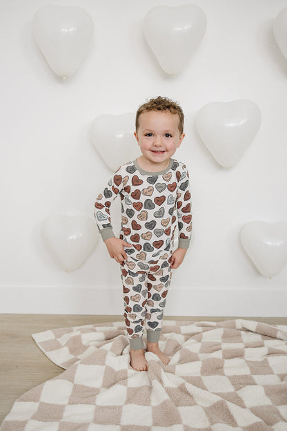 Child wearing a heart-patterned pajama set standing on a checkered blanket with a heart-shaped balloon background.