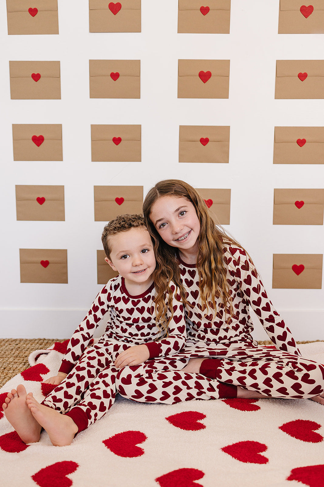 Two children in matching heart-patterned pajamas sitting on a floor with heart-themed decor.