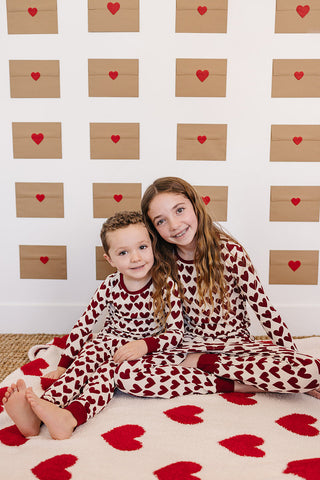 Two children in matching heart-patterned pajamas sitting on a floor with heart-themed decor.