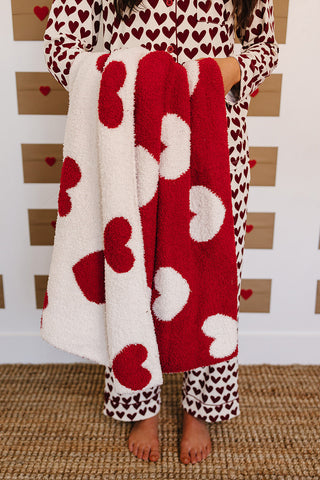 Person wearing a heart-patterned robe and pajama set on a textured floor.